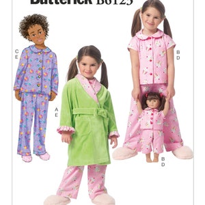 May include: A sewing pattern for pajamas and a robe for children and a doll. The pattern is called Butterick B6123. The pajamas are pink and purple with a cupcake print. The robe is green with a pink trim. The doll is wearing a pink and purple cupcake print pajamas.