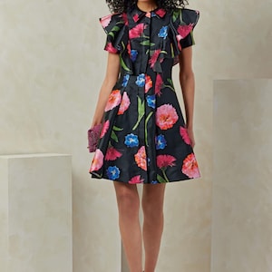 Puede incluir: Un vestido negro de estampado floral con cuello de volantes y mangas cortas. El vestido tiene un cierre de botones en la parte delantera y una falda acampanada.
