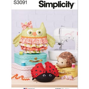 May include: Simplicity sewing pattern S3091 featuring stuffed animal designs. The image shows an owl, ladybug, and hedgehog. The owl has a bow and layered ruffles. The ladybug is red and black. The hedgehog is brown and tan. The text "easy-to-sew" is visible.