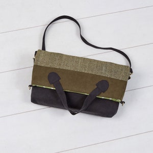 May include: A multi-toned tote bag with a black shoulder strap and handles. The bag features a color block design with sections of olive green, dark green, and black fabric. The top section is a textured olive green material.
