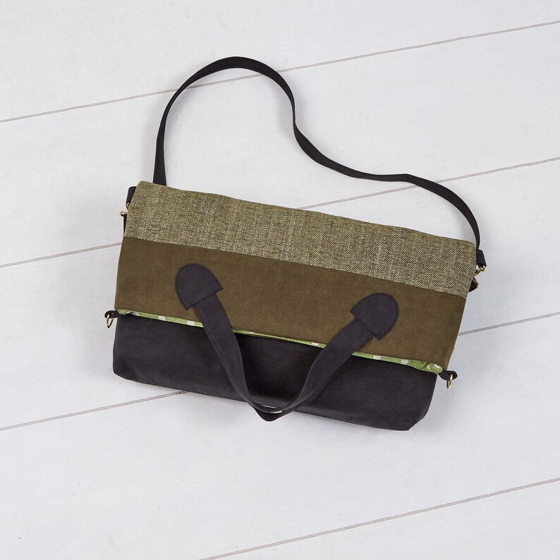 May include: A multi-toned tote bag with a black shoulder strap and handles. The bag features a color block design with sections of olive green, dark green, and black fabric. The top section is a textured olive green material.