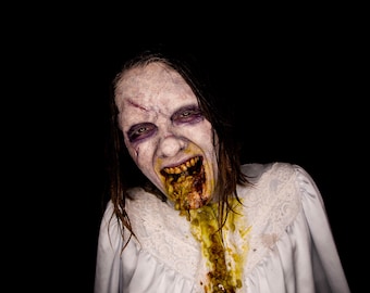 Peut inclure: Une femme à la peau pâle et aux cheveux foncés est vêtue d'une robe blanche à bordure de dentelle. Sa bouche est grande ouverte, révélant des dents jaunes et un filet de vomi vert et jaune qui coule le long de son menton et de sa poitrine.