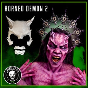 May include: A white plastic prosthetic demon mask with horns, a mouth, and eye holes. The mask is next to a person wearing a purple demon makeup with horns and a crown. The person is wearing a black wig and has a fierce expression.
