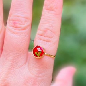 May include: A gold ring with a red circular stone containing a small dried flower
