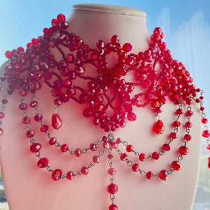 May include: A red beaded choker necklace with a delicate, intricate design. The necklace features multiple strands of beads and dangling drops, creating a layered and elegant look.