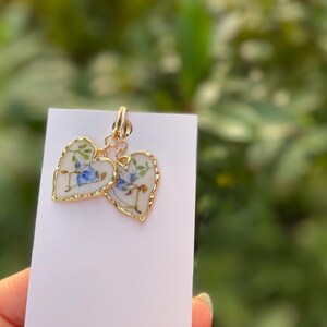 May include: A pair of gold heart-shaped earrings with a white background and blue floral designs.