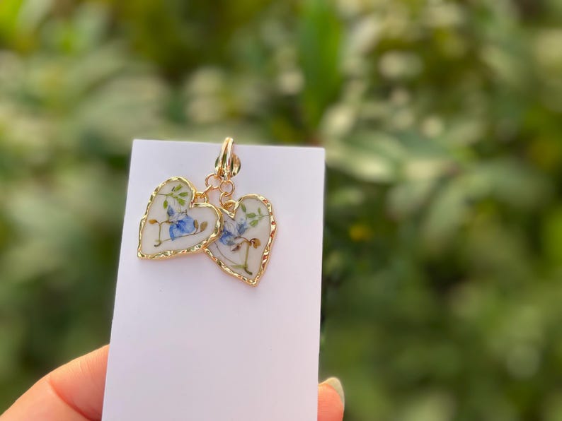 May include: A pair of gold heart-shaped earrings with a white background and blue floral designs.