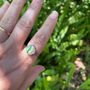 May include: A silver ring with a round, clear resin setting featuring a green leaf and white flowers.