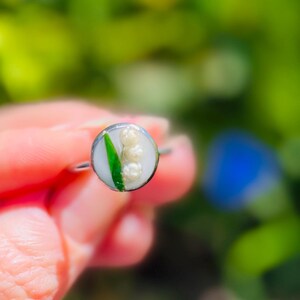 May include: A silver ring featuring a white and green lily of the valley flower design.