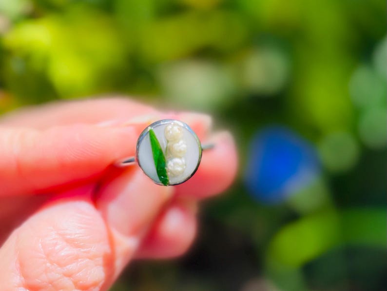 May include: A silver ring featuring a white and green lily of the valley flower design.