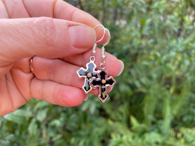 May include: A pair of silver dangle earrings with black cross charms. Each cross has a small gold dot in the center.