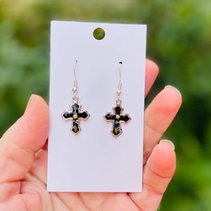 May include: A pair of silver dangle earrings with black cross charms. Each cross has a small gold dot in the center.