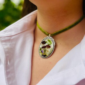 K&ouml;nnte beinhalten: Eine gr&uuml;ne Samt-Chokerkette mit einem silbernen ovalen Anh&auml;nger mit gepressten Blumen und Pilzen.
