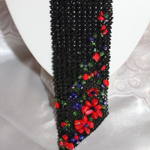 May include: A black beaded necklace with a floral design. The necklace features red, green, and blue gemstone accents. The necklace is displayed on a white mannequin head.
