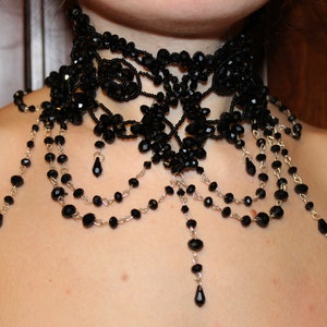 May include: A black beaded choker necklace with multiple strands of beads and dangling drops. The necklace is made of small black beads and silver chain.