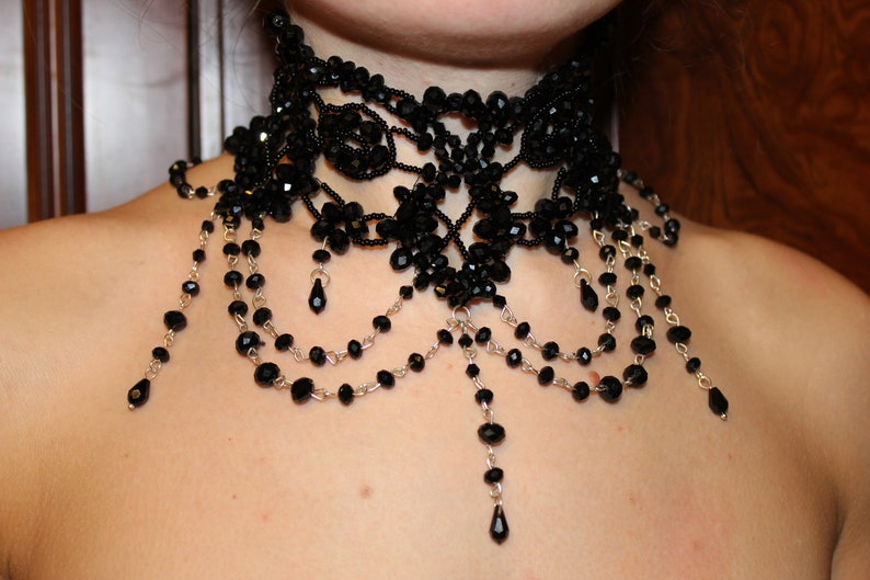 May include: A black beaded choker necklace with multiple strands of beads and dangling drops. The necklace is made of small black beads and silver chain.