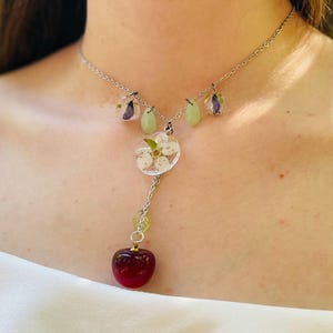 May include: A silver chain necklace with a cherry charm, a flower charm, and two green teardrop charms.
