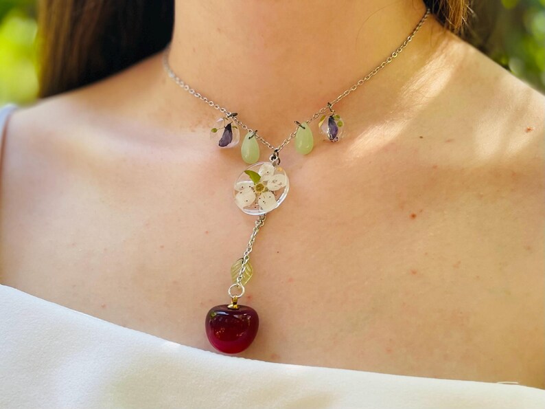 May include: A silver chain necklace with a cherry charm, a flower charm, and two green teardrop charms.