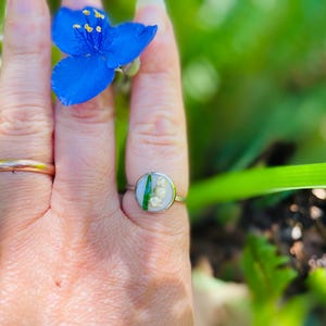 May include: A silver ring with a round, clear resin setting featuring a pressed lily of the valley flower and a green leaf.