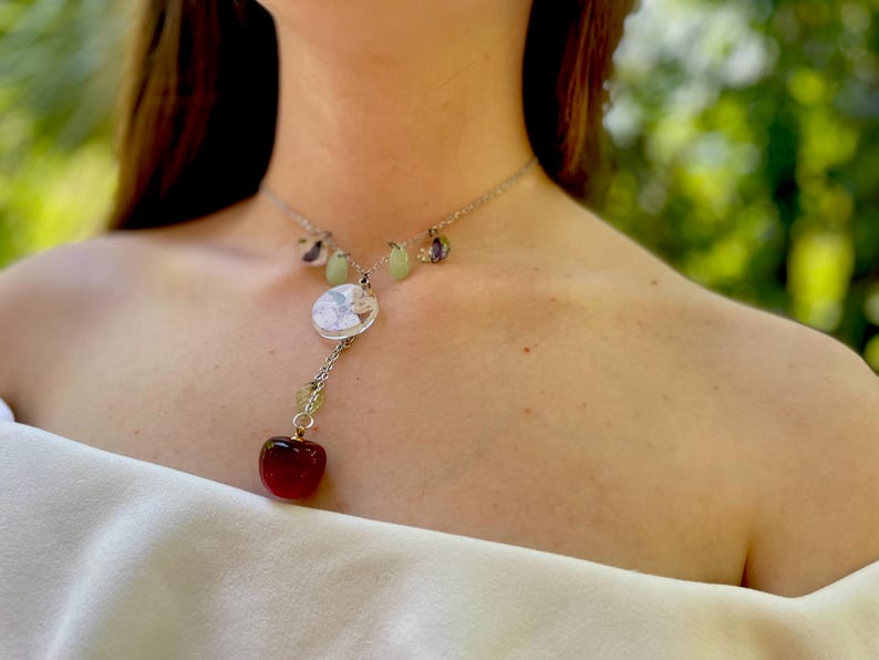 May include: A silver necklace with a red heart charm, a round white charm, and green and purple beads.