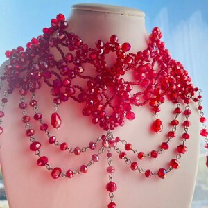 May include: A red beaded choker necklace with a delicate, intricate design. The necklace features multiple strands of beads and a dangling pendant.