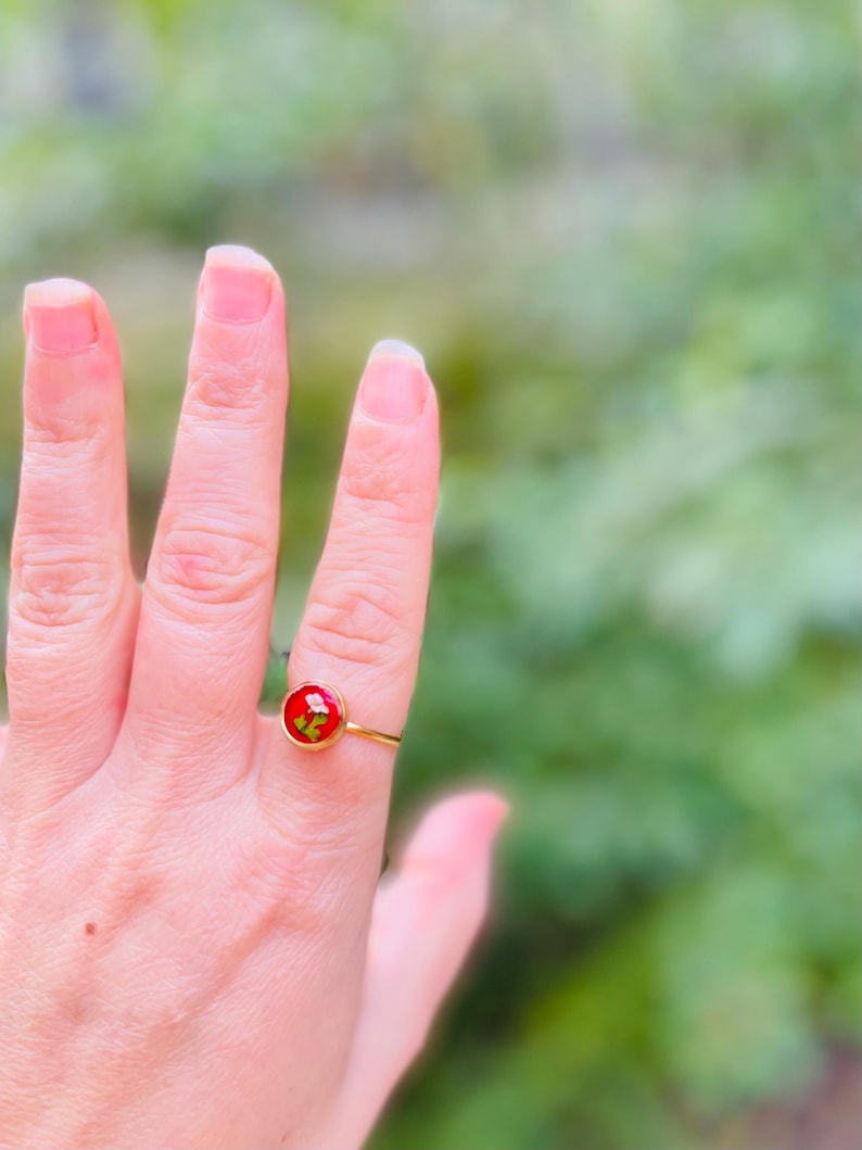 May include: A gold ring with a red circular stone containing a small dried flower