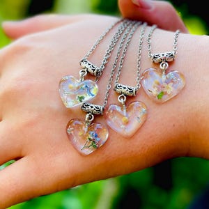 Puede incluir: Cuatro collares de plata con colgantes en forma de coraz&oacute;n transparentes llenos de flores prensadas. Las flores son blancas, amarillas y azules.