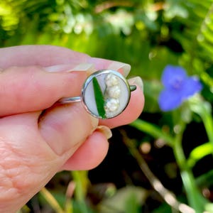 May include: A silver ring with a white and green resin inlay featuring a cluster of white lily of the valley flowers.