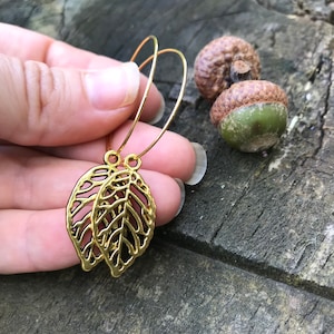 Puede incluir: Pendientes de aro dorados con un delicado diseño de hojas. Las hojas están recortadas y tienen un patrón de filigrana.
