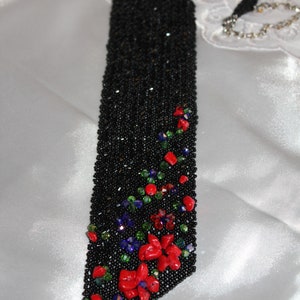 May include: A black beaded evening bag with a floral design. The bag is rectangular with a long, beaded strap. Red, green, and blue beads form a floral pattern on the lower portion of the bag.