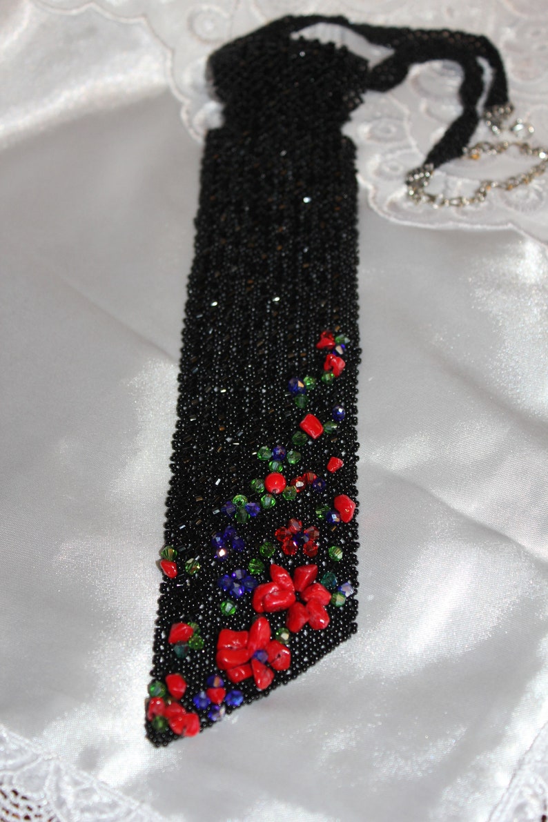 May include: A black beaded evening bag with a floral design. The bag is rectangular with a long, beaded strap. Red, green, and blue beads form a floral pattern on the lower portion of the bag.