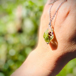 May include: A silver chain necklace with a clear pendant containing pressed green leaves and flowers.