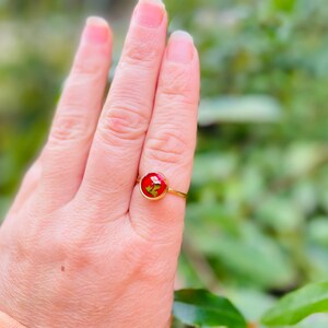 May include: A gold ring with a red resin cabochon featuring a pressed flower design.