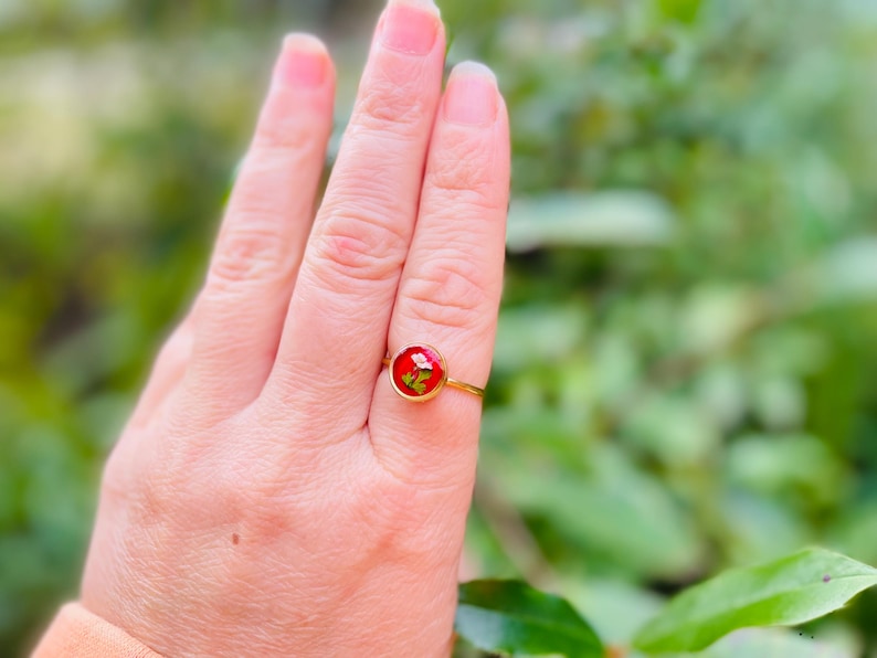 May include: A gold ring with a red resin cabochon featuring a pressed flower design.