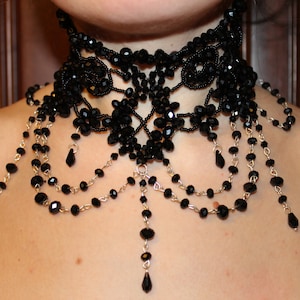 May include: A black beaded choker necklace with a delicate, intricate design. The necklace features multiple strands of beads and a dangling pendant.