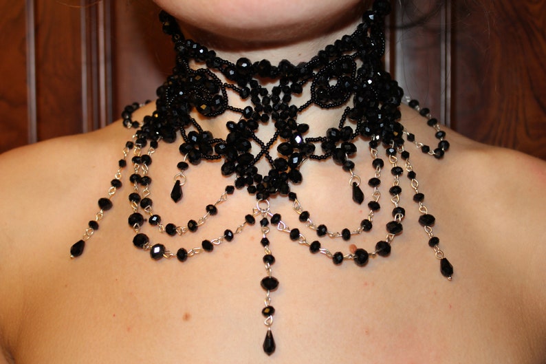 May include: A black beaded choker necklace with a delicate, intricate design. The necklace features multiple strands of beads and a dangling pendant.