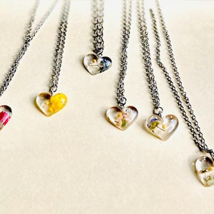 Puede incluir: Seis collares de cadena plateada con colgantes en forma de coraz&oacute;n. Cada colgante est&aacute; lleno de flores prensadas y resina transparente. Las flores son en tonos de rosa, amarillo, azul y blanco.