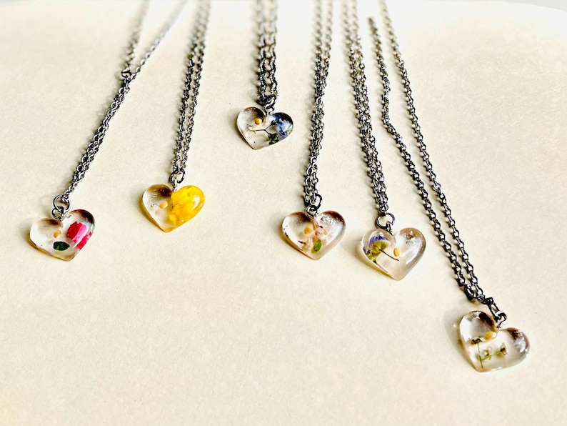 Puede incluir: Seis collares de cadena plateada con colgantes en forma de coraz&oacute;n. Cada colgante est&aacute; lleno de flores prensadas y resina transparente. Las flores son en tonos de rosa, amarillo, azul y blanco.