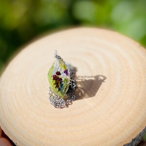 May include: A silver chain necklace with a clear green pendant containing pressed flowers and leaves.