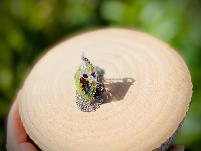May include: A silver chain necklace with a clear green pendant containing pressed flowers and leaves.