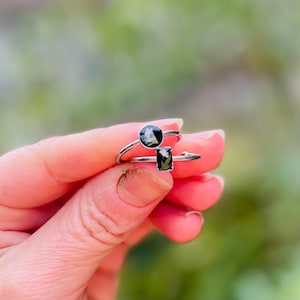 May include: Two silver rings with black and white stones. The ring on the left has a round stone, and the ring on the right has a rectangular stone.
