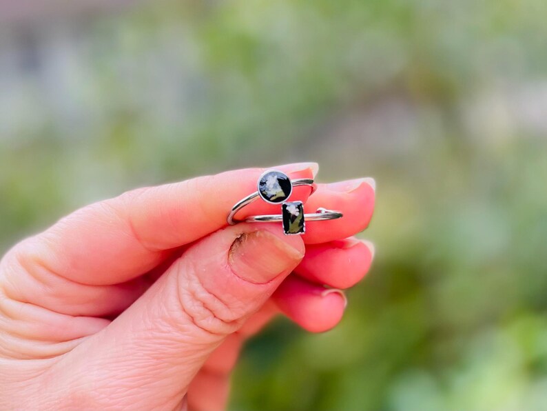 May include: Two silver rings with black and white stones. The ring on the left has a round stone, and the ring on the right has a rectangular stone.