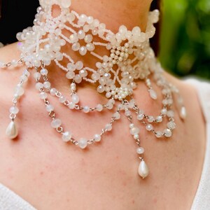 May include: A white beaded choker necklace with a delicate floral design and dangling pearl accents.