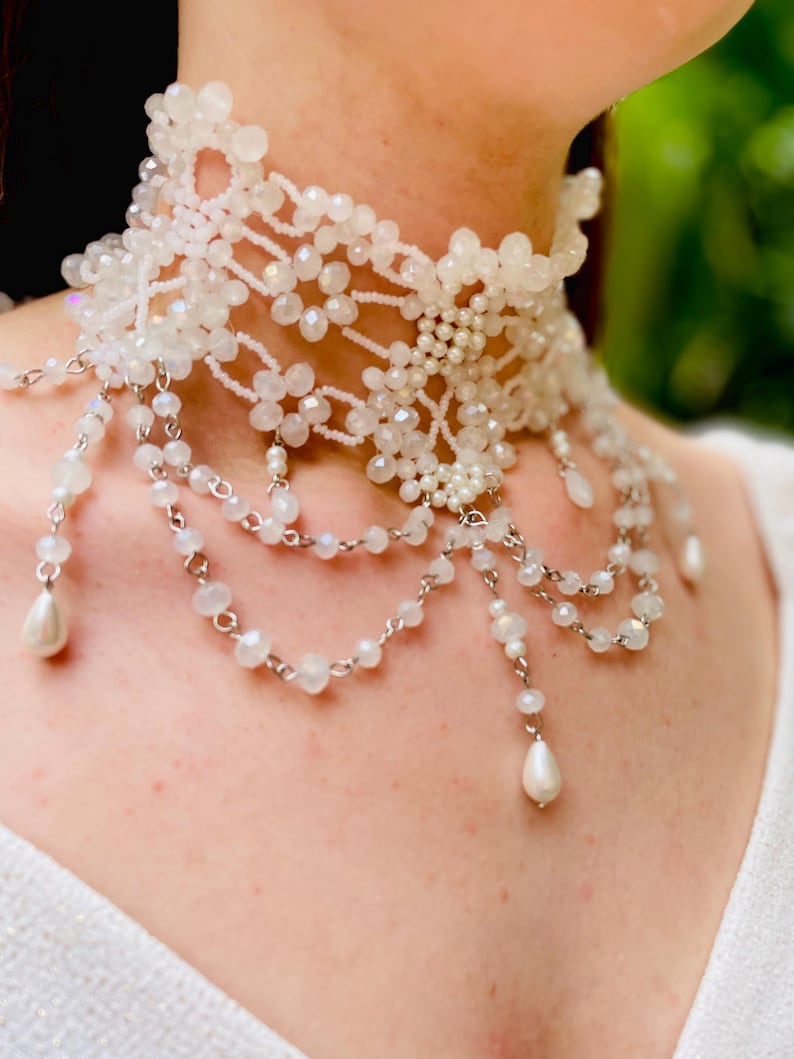 May include: A white beaded choker necklace with a delicate floral design and dangling pearl accents.