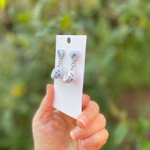 以下が含まれることがあります： 青と白の磁器のデザインのドロップイヤリングのペア。イヤリングは上部にハート型、下部に涙型をしています。