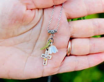 May include: A silver chain necklace with a silver cross charm, a white flower charm, and a green leaf charm.