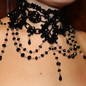 May include: A black beaded choker necklace with multiple strands of beads and dangling drops. The necklace is made of black beads and silver chain.