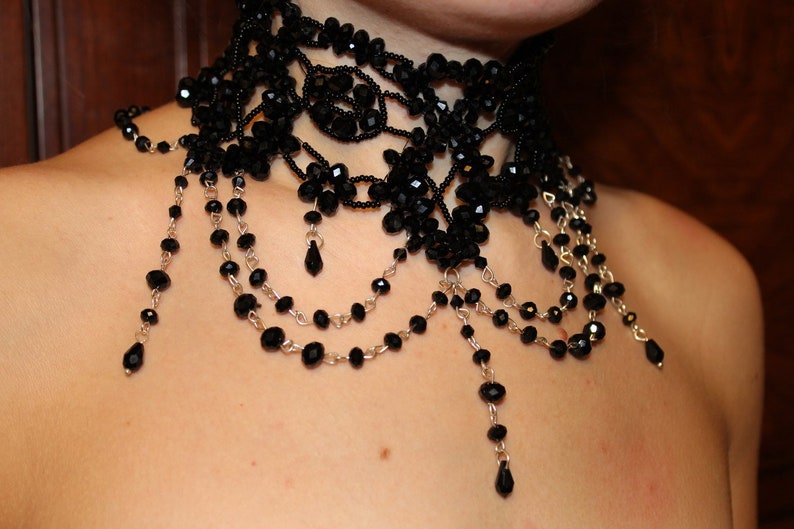 May include: A black beaded choker necklace with multiple strands of beads and dangling drops. The necklace is made of black beads and silver chain.