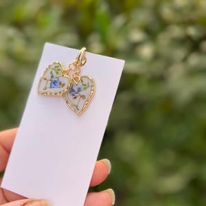 May include: A pair of gold heart-shaped earrings with a floral design. The earrings are made of white porcelain with blue and green flowers.