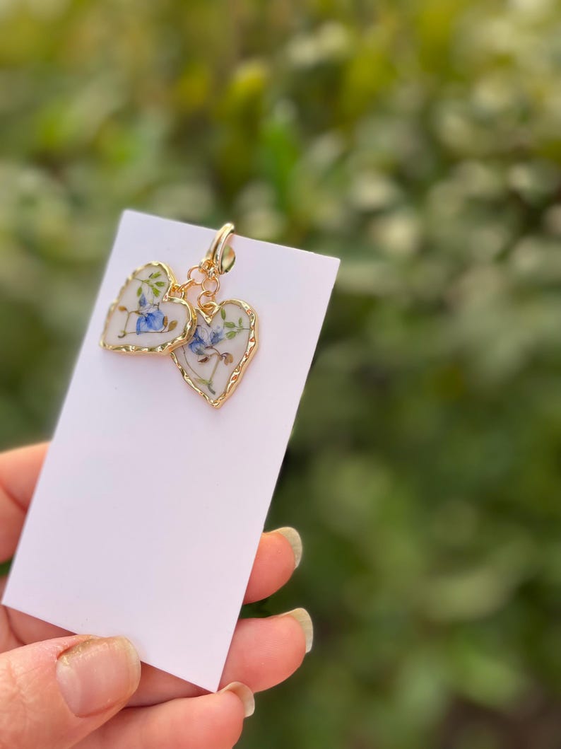 May include: A pair of gold heart-shaped earrings with a floral design. The earrings are made of white porcelain with blue and green flowers.